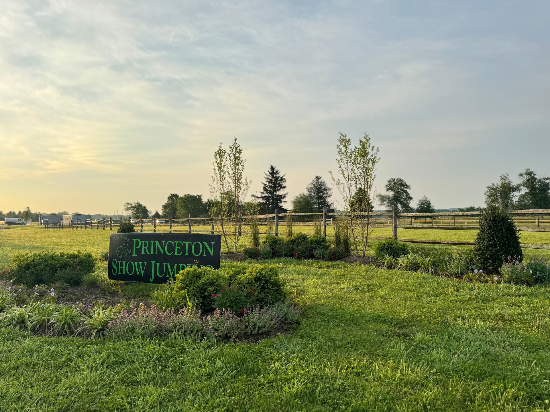 A sign for princeton show jumping is in the middle of a grassy field.