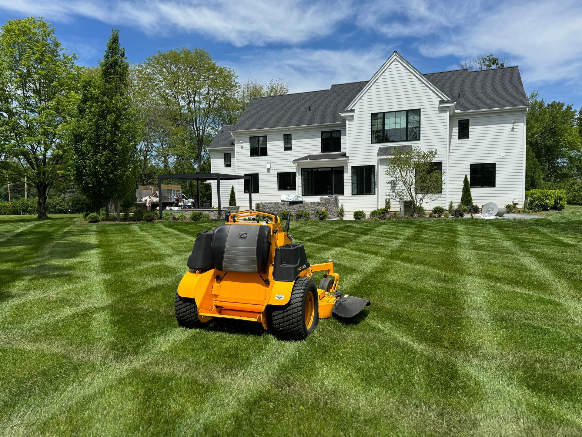 A yellow lawn mower is cutting the grass in front of a large white house.