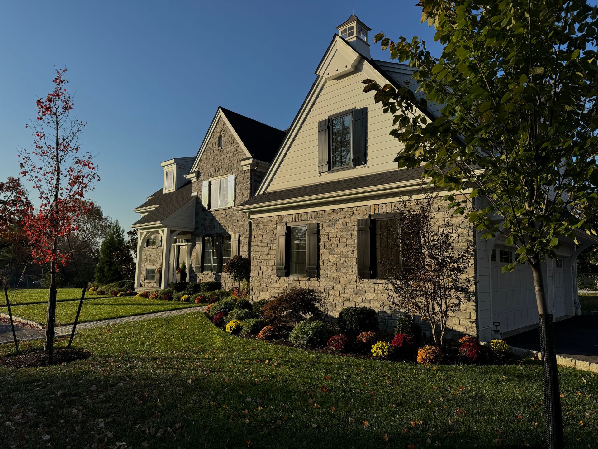 A large white house with black shutters sits on a lush green lawn.