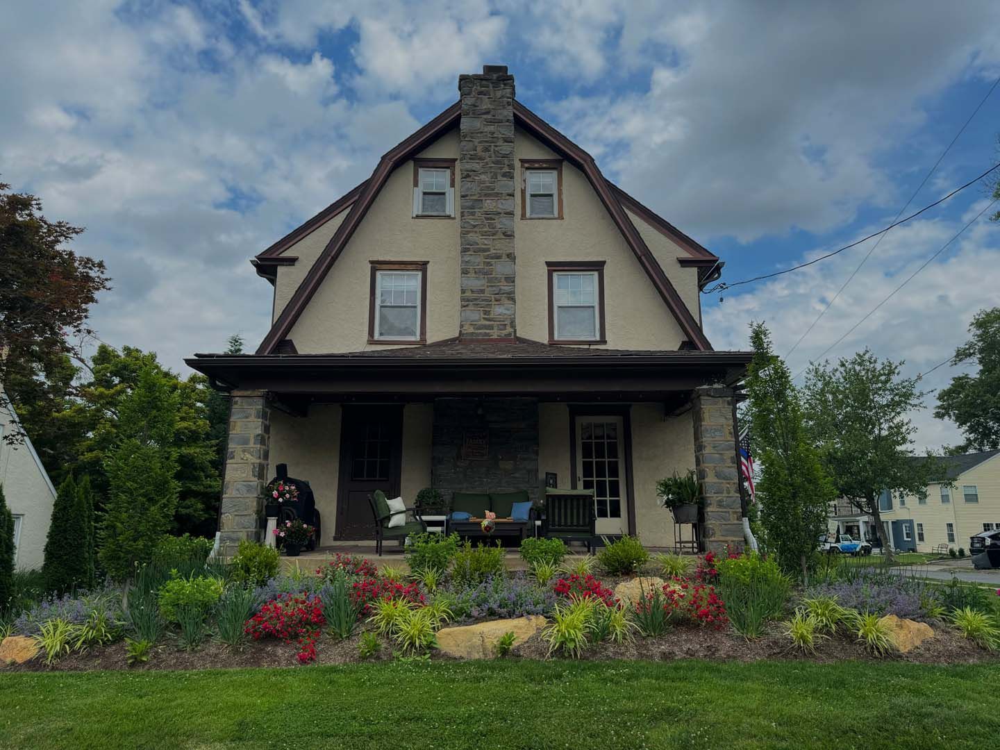A large house with a stone chimney and a lush green lawn in front of it.