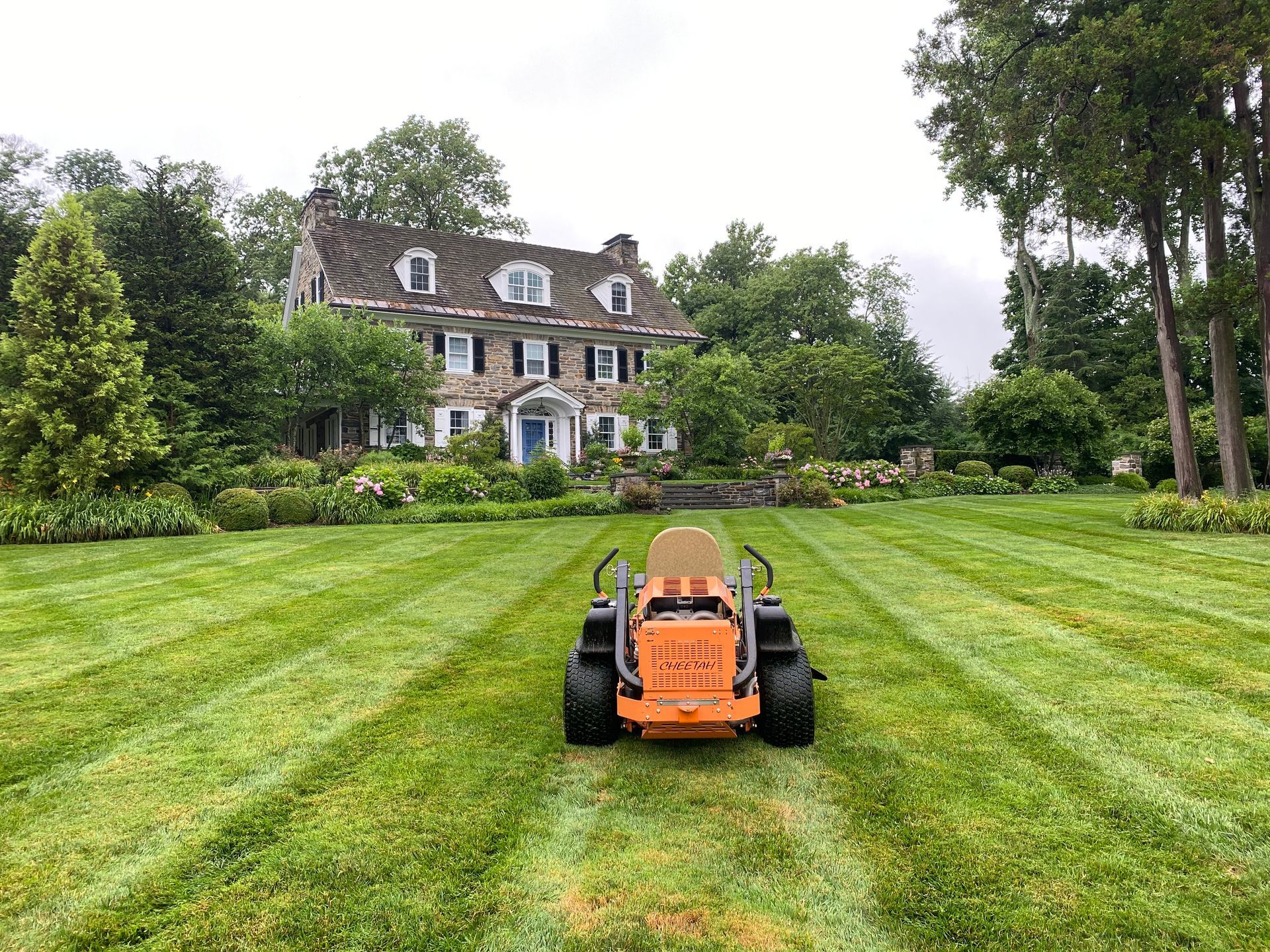A lawn mower is cutting the grass in front of a large house.