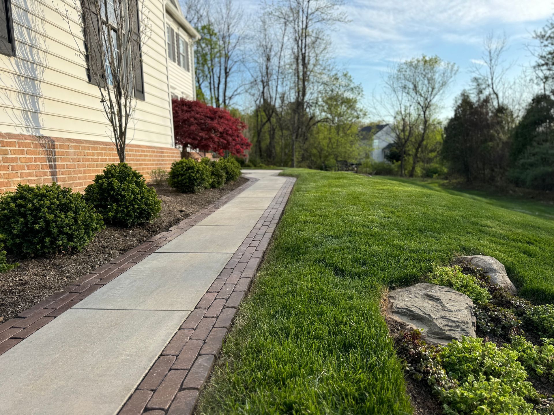 A brick walkway leading to a house with a lush green lawn.