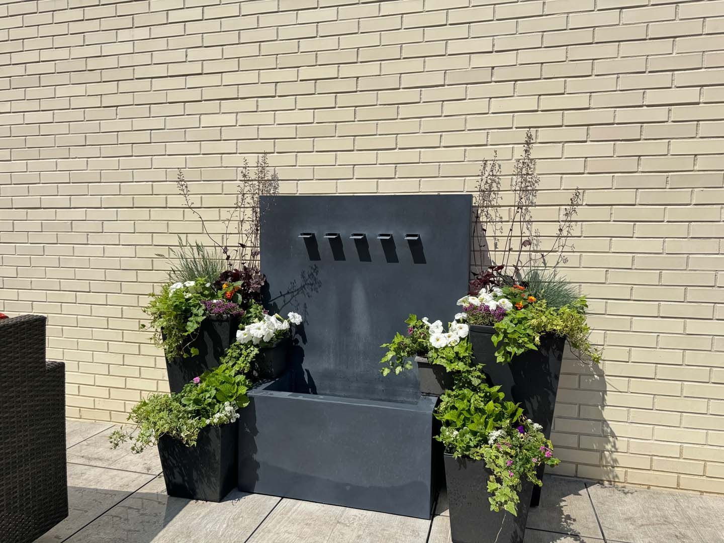 A fountain is surrounded by potted plants in front of a brick wall.