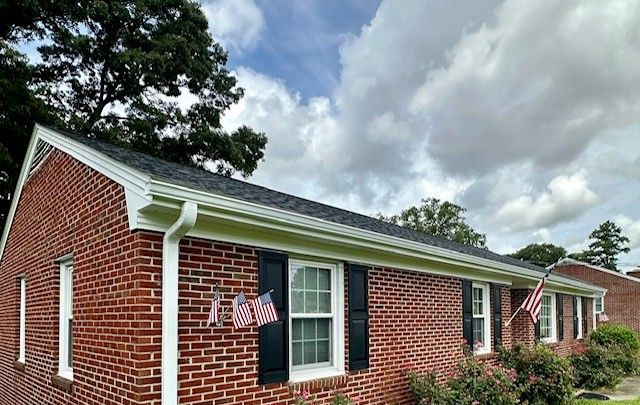 Red brick two-story house with white trim, black shutters, and a small porch. A flag hangs near the front door.