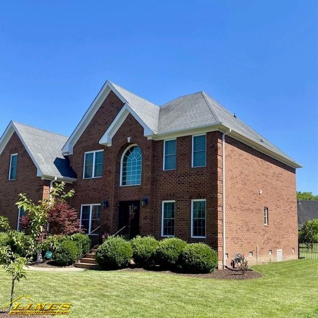Brick house with gray roof under a blue sky, lush green lawn, and trimmed bushes.