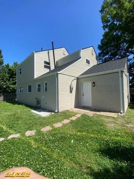Beige two-story house with black roof, white door, green grass and blue sky.