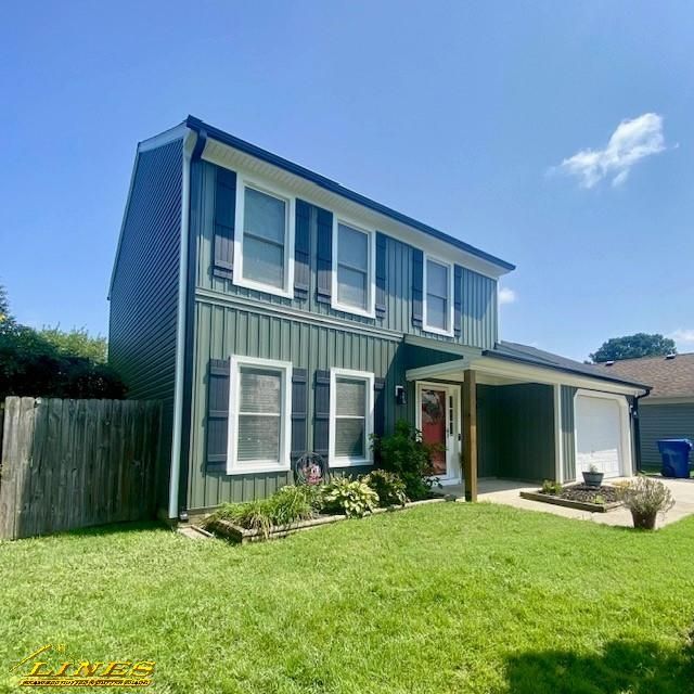 Green two-story house with white window frames, black shutters, and a green lawn under a blue sky.