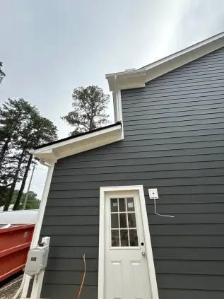 Gray house siding with white trim, door, and gutters. Exterior shot on a cloudy day.