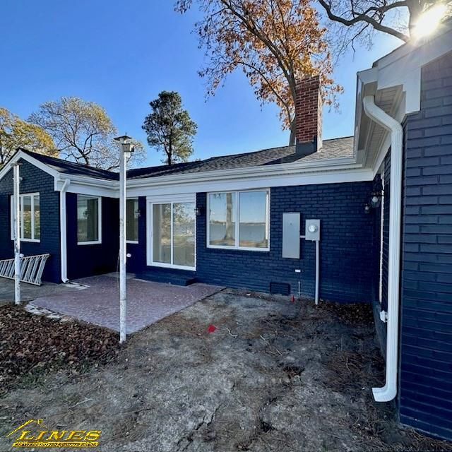Exterior view of a dark blue brick house with white trim, a red brick chimney, and a patio.