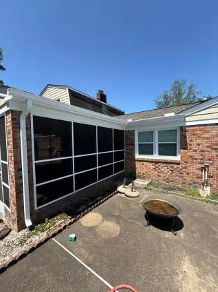 Screened-in porch with white trim and black screens attached to a brick house. Fire pit in the foreground.