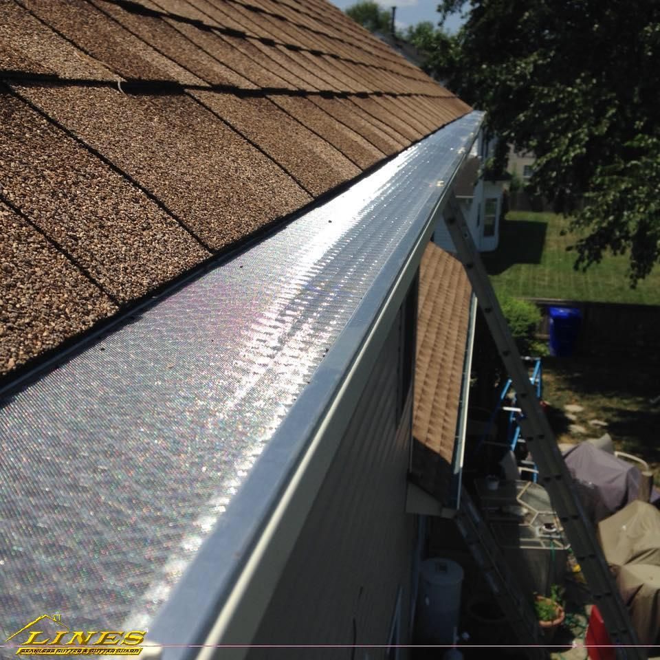 Close-up of a gutter with a metallic mesh cover on a house roof, with a ladder nearby.