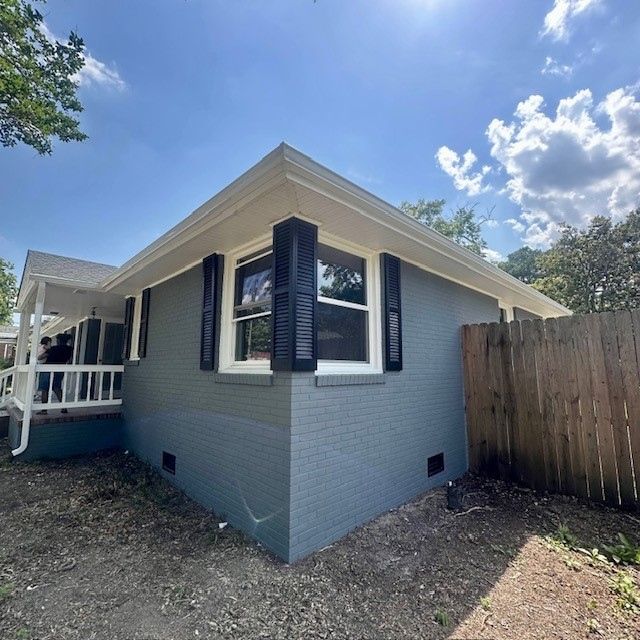 Gray painted brick house with black shutters, white trim, and wooden fence.