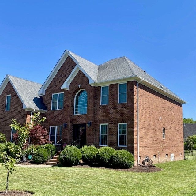 Two-story brick house with manicured lawn, blue sky.