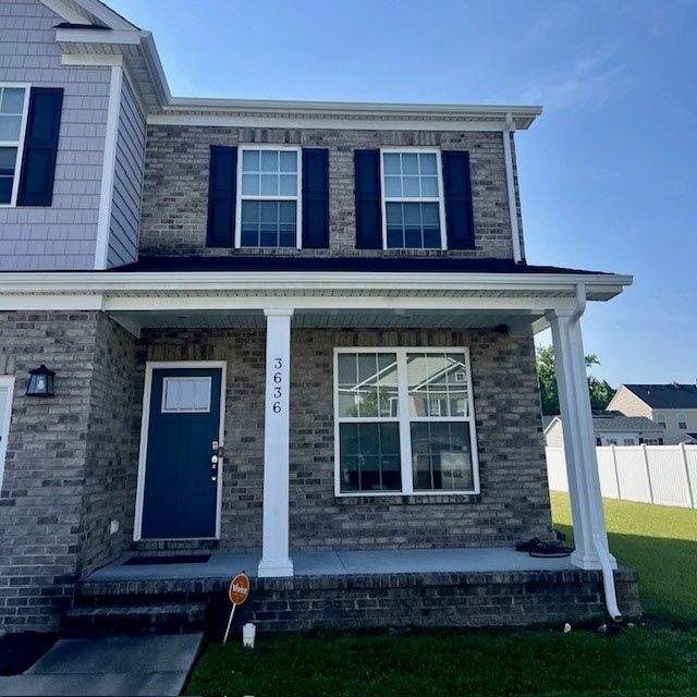 Two-story brick house with dark shutters, blue door, and white trim, on a sunny day.