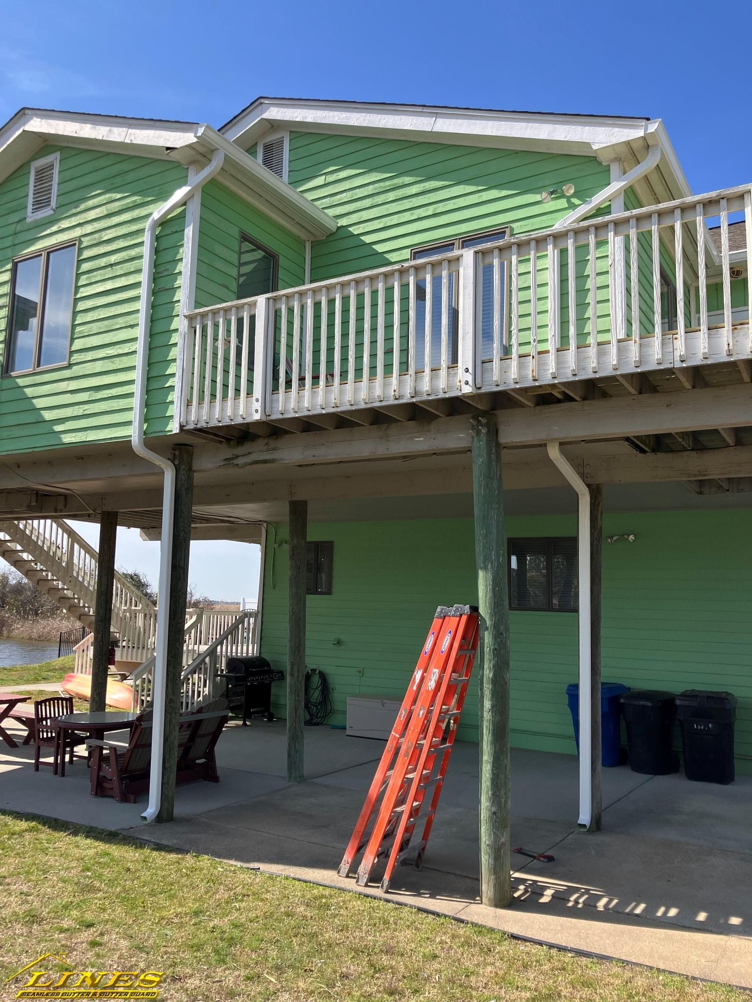 Green house on stilts with a deck. A red ladder is propped against a support beam.