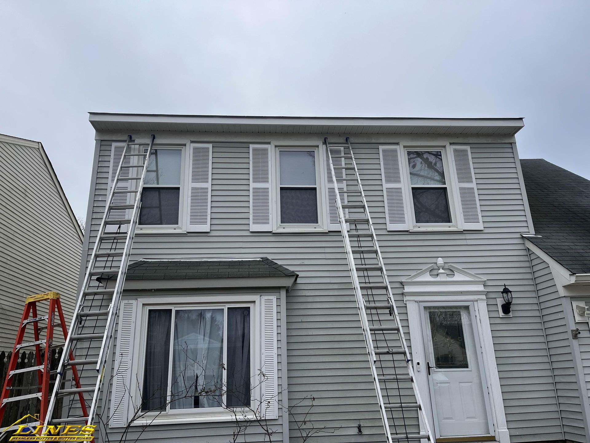 House with two ladders, shutters, and a cloudy sky.