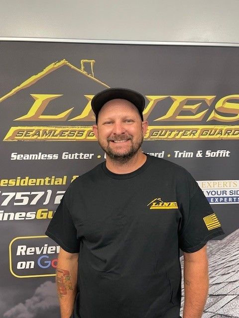Man wearing a black shirt and hat in front of a business banner. The banner promotes seamless gutters and gutter guards.