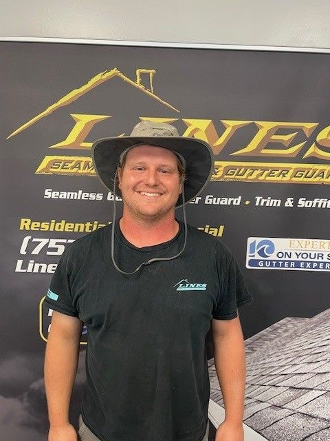 Man in a hat smiling in front of a business sign for seamless gutters.