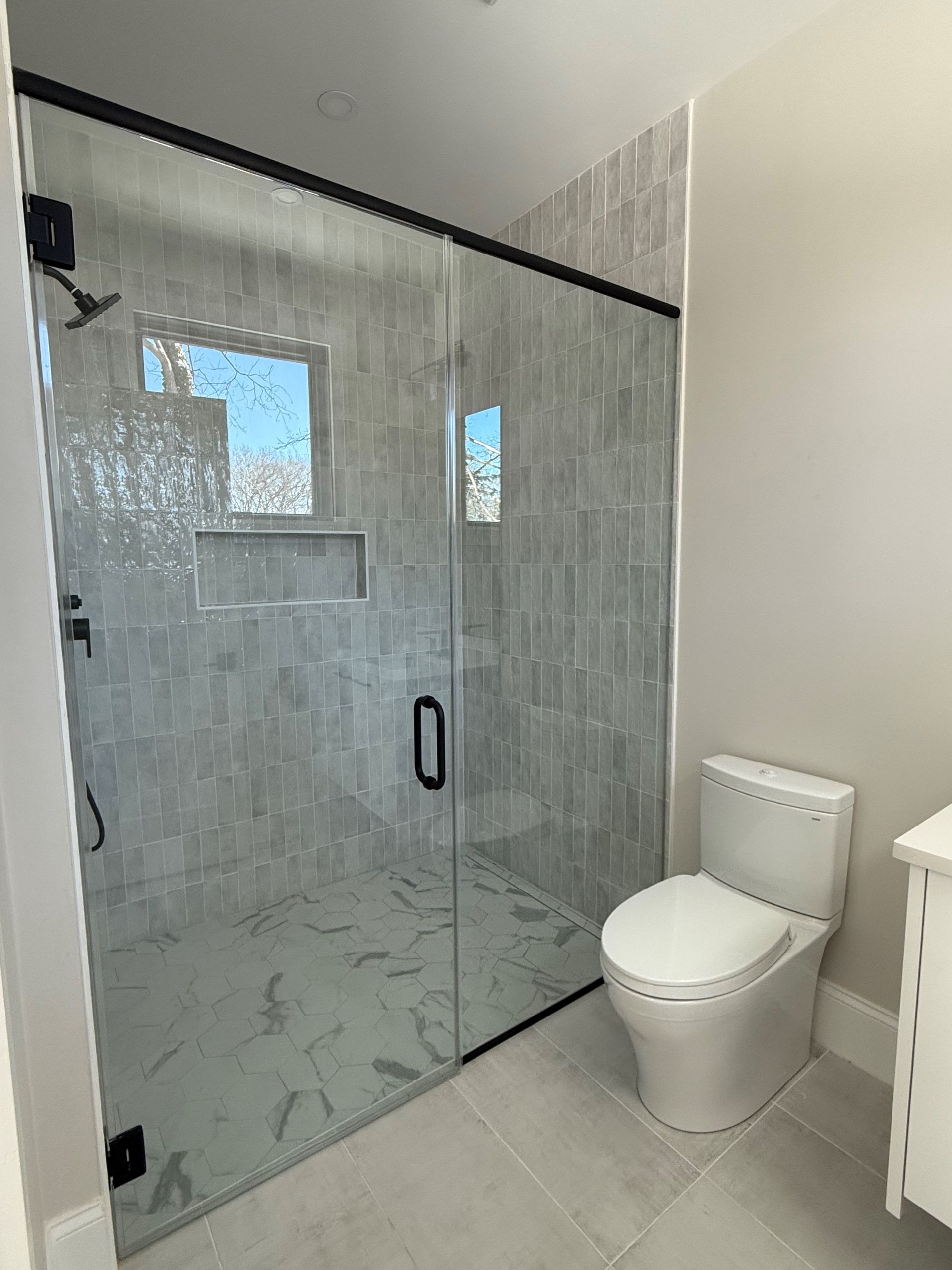 A bathroom with a toilet , shower and glass door.