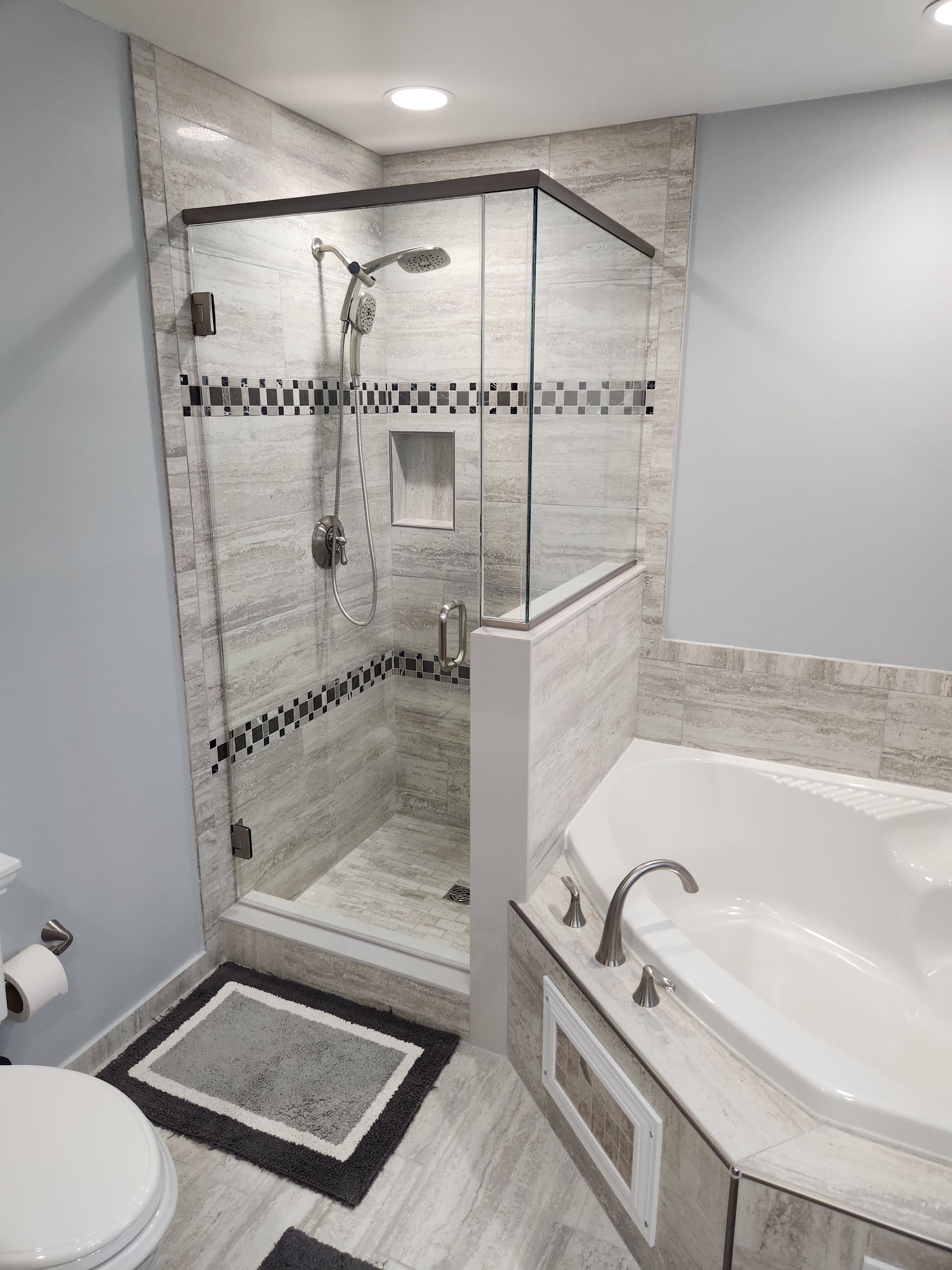 A bathroom with a walk in shower , tub , toilet and shower stall.