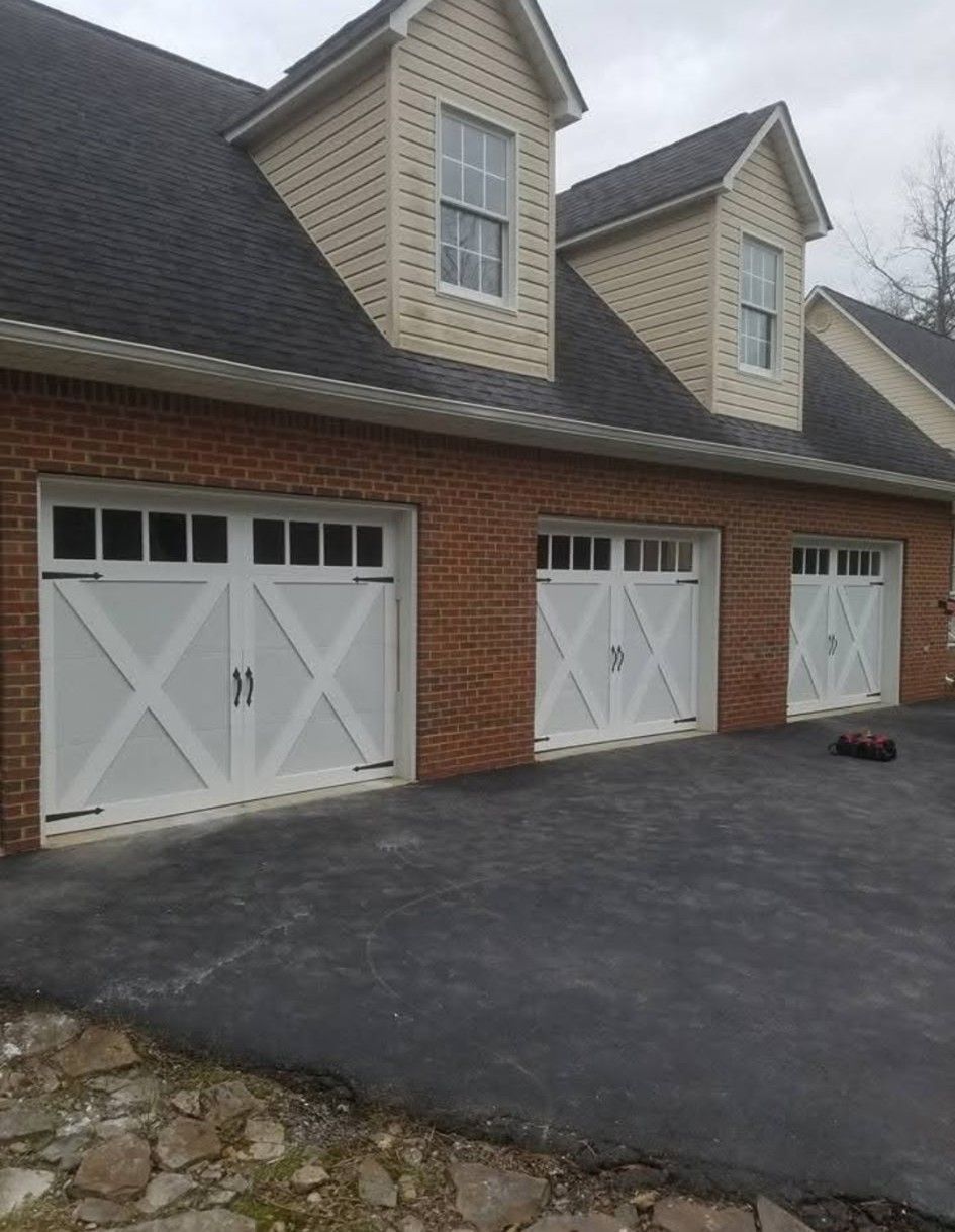 Three white garage doors with decorative X patterns on a brick building, dormer windows overhead.