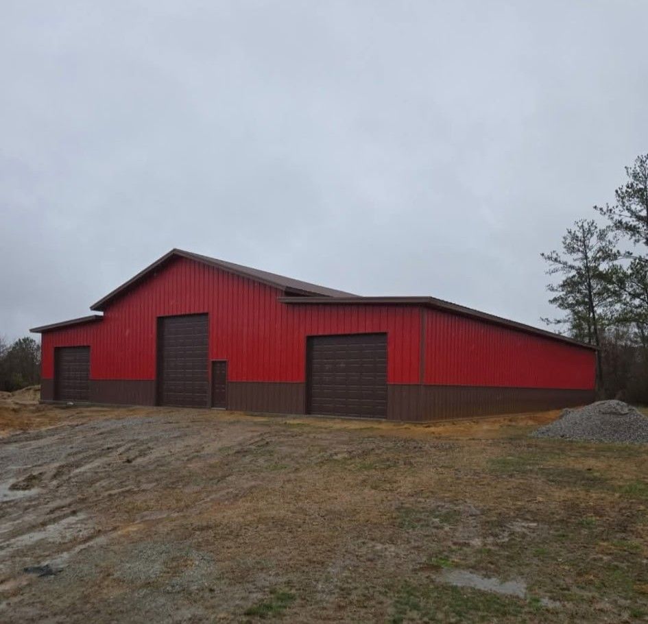 Red and brown barn with three garage doors on a cloudy day.