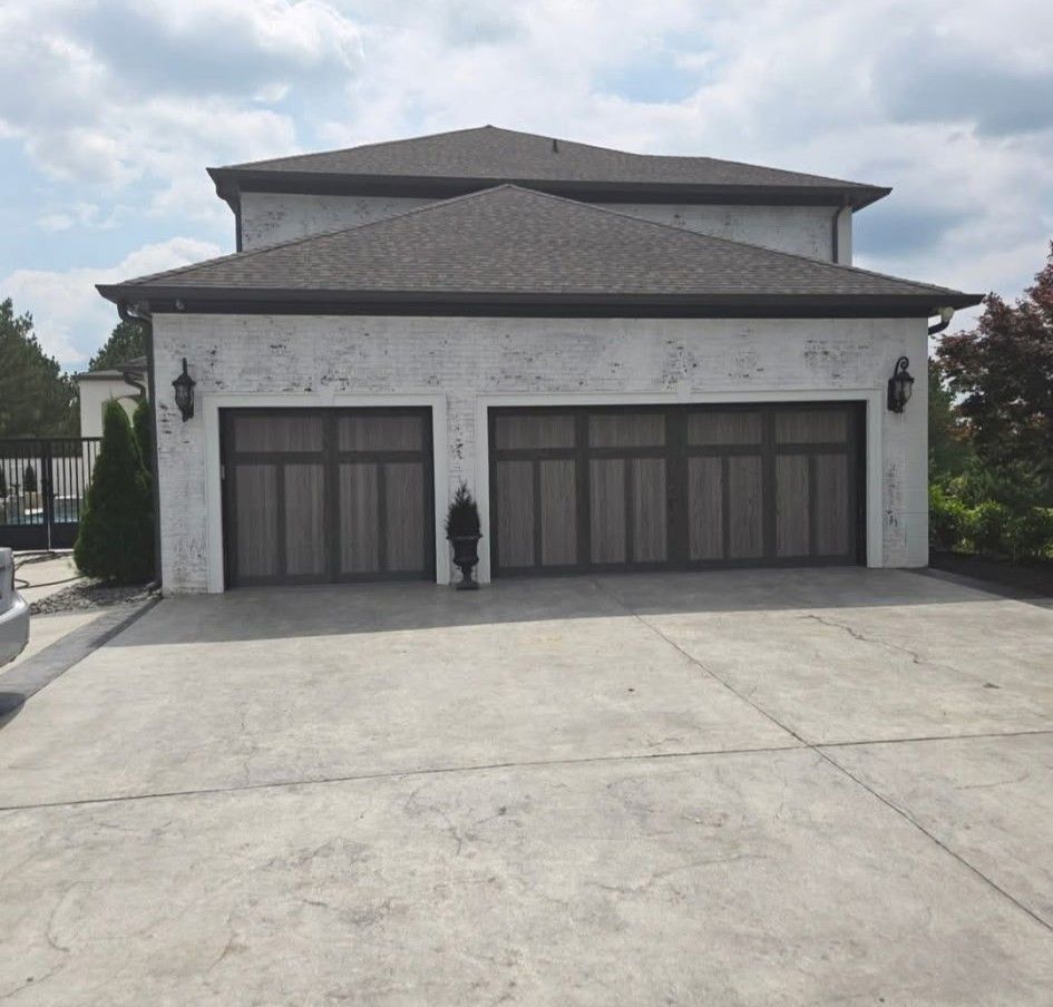 Two-car garage with dark wooden doors on a light stucco house under a cloudy sky.