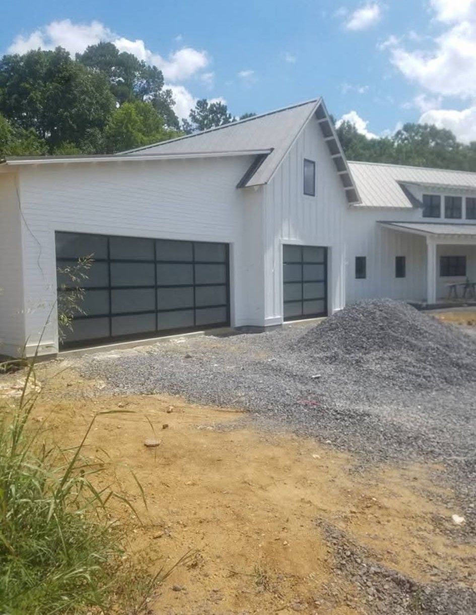 White house with two glass garage doors, gray gravel pile, and a blue sky.