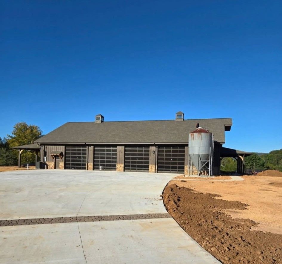 Barn-style building with clear garage doors, concrete driveway, and silo under a clear blue sky.