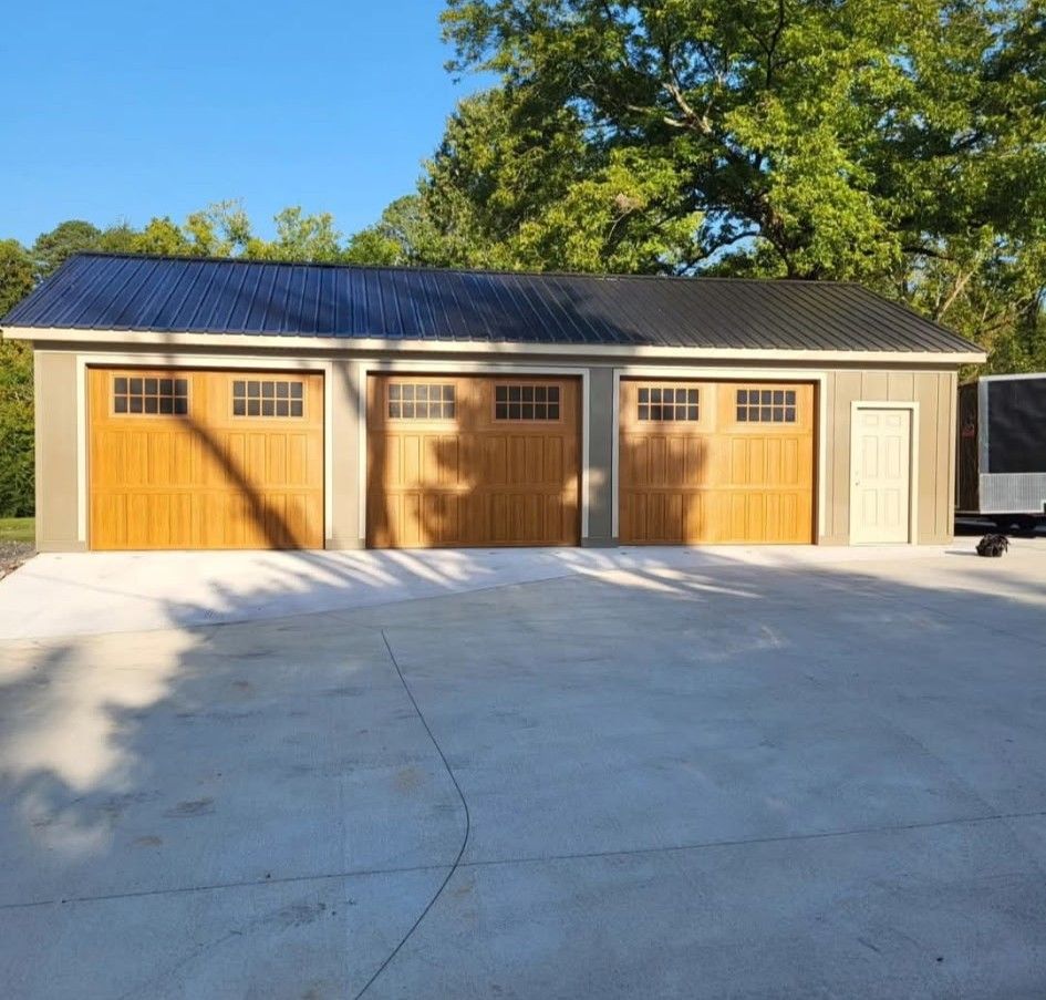 Three-car garage with wooden doors, black metal roof, and concrete driveway.
