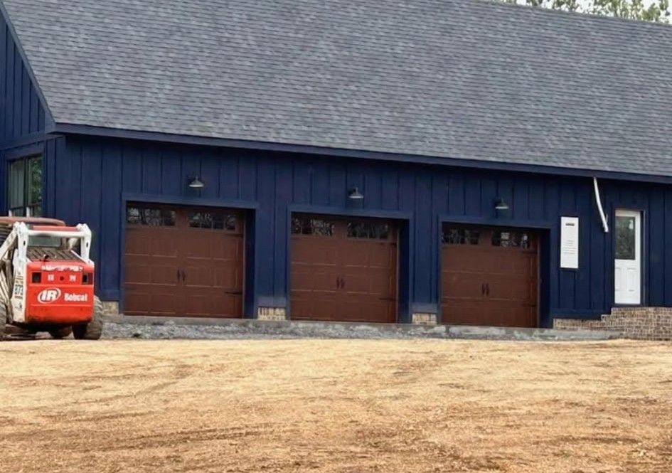 Blue building with brown garage doors; small tractor nearby, dirt ground.