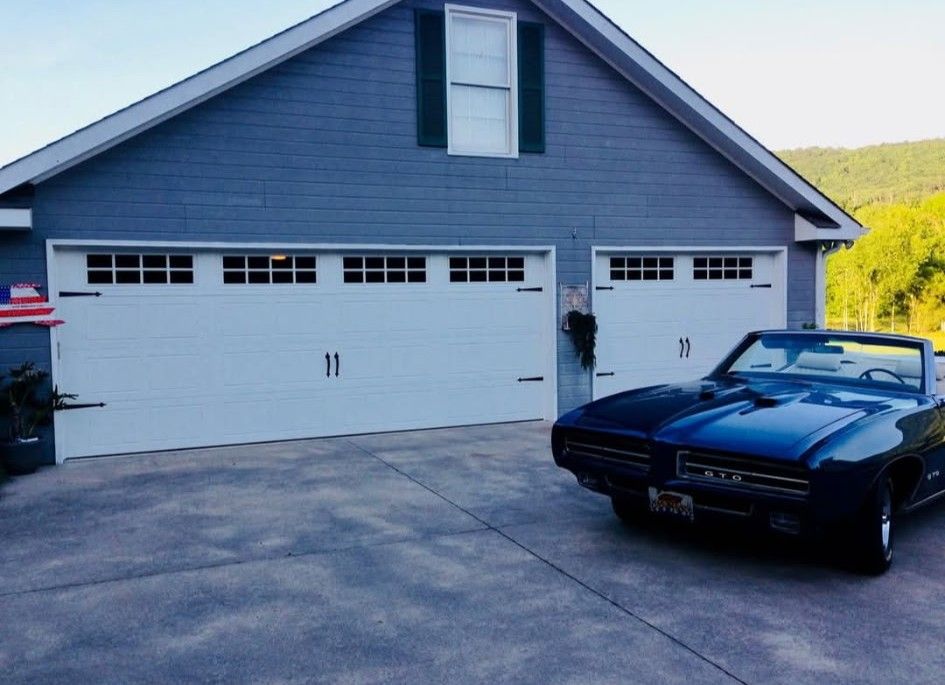 Blue convertible parked in front of a two-car garage with white doors; mountains visible in the background.