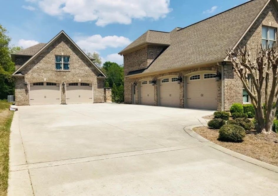 Two brick garages with beige doors and a long concrete driveway under a blue sky.