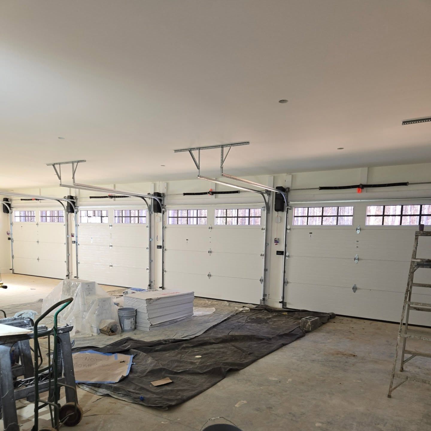 Interior view of a garage with four white garage doors installed, construction materials on the floor.