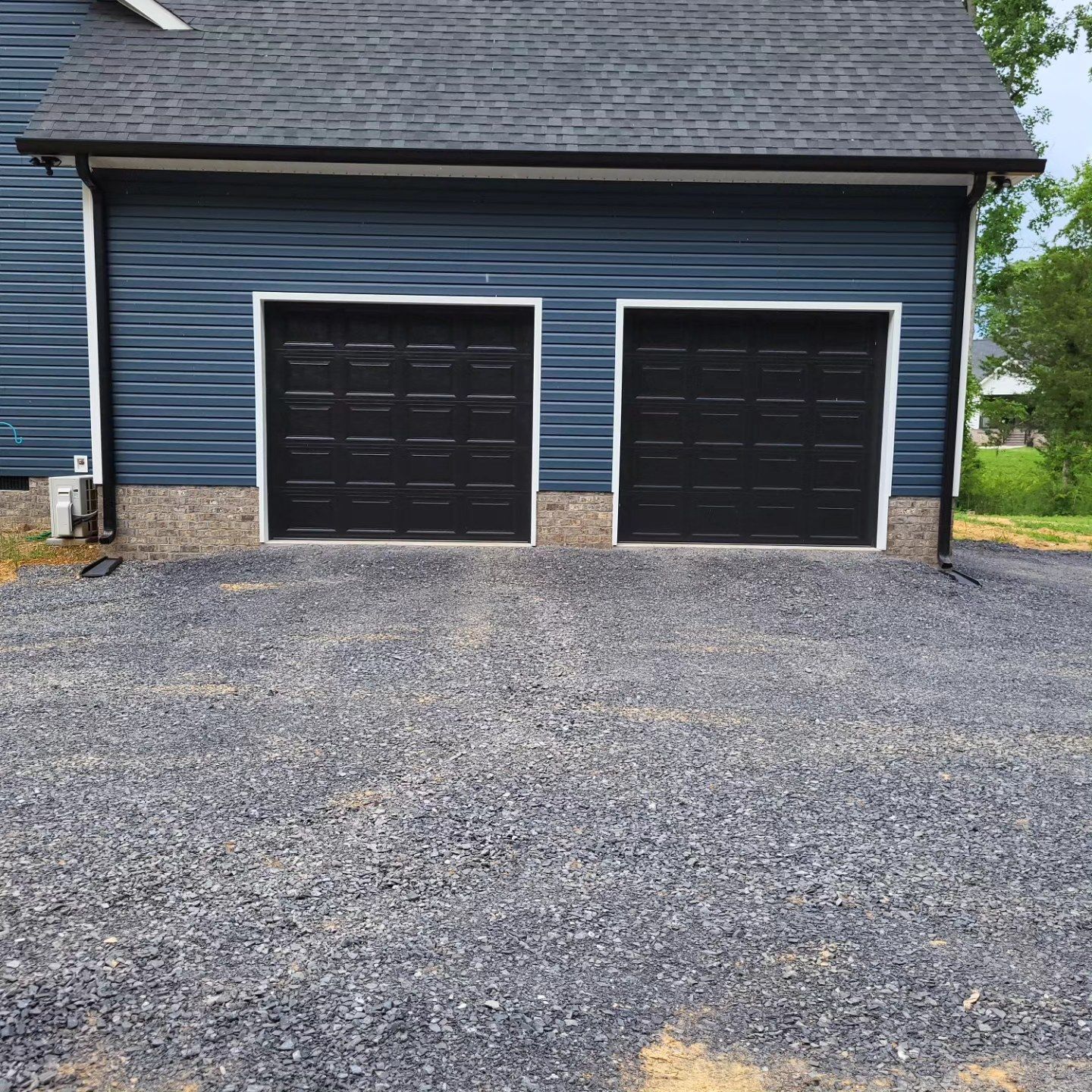 Blue garage with two black doors, gravel driveway.