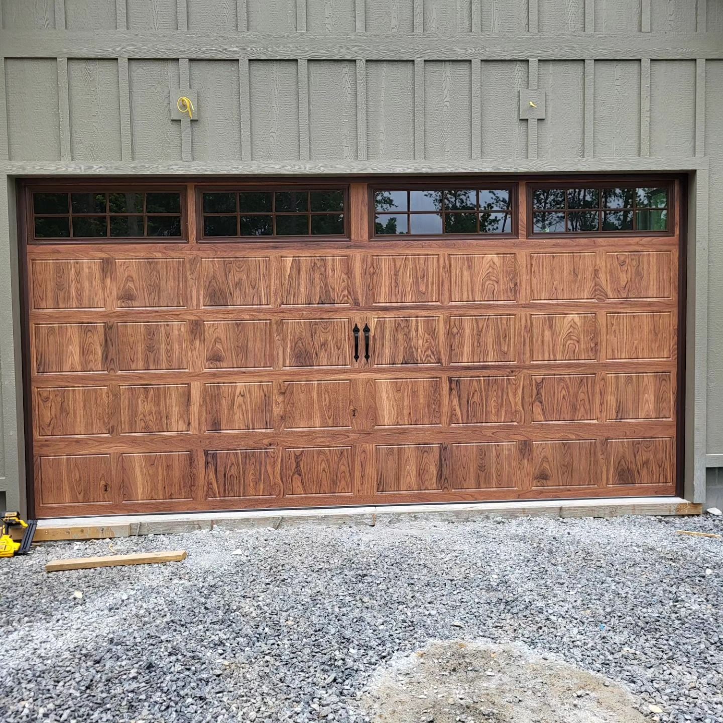 Wooden garage door with glass windows, set in gravel, against a grey building facade.