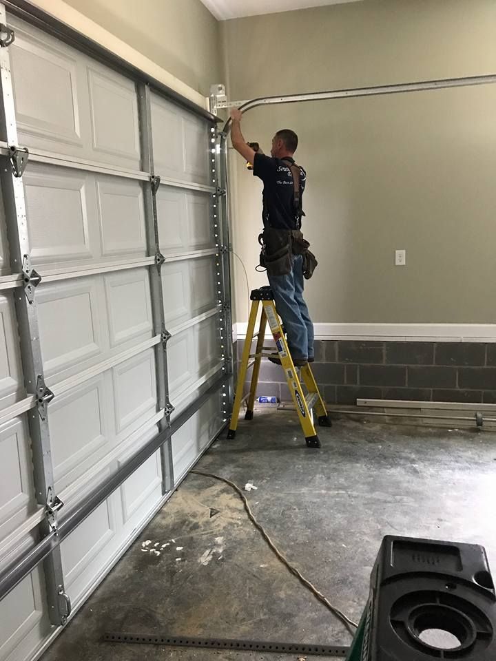 A man on a ladder installs a garage door track in a garage.