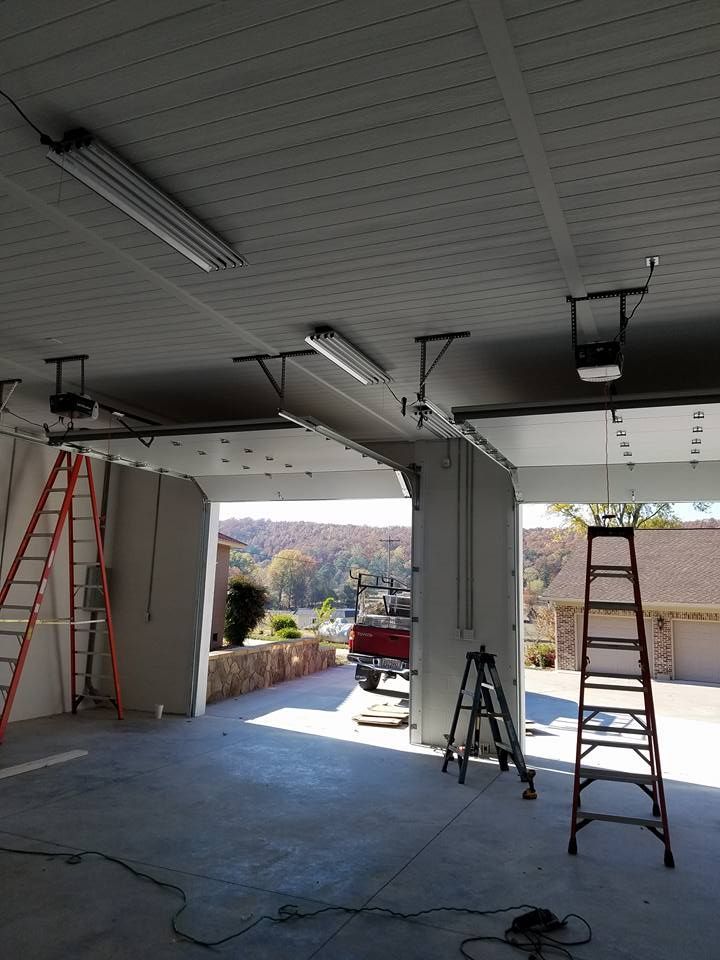 Garage interior during construction; ladders, open doorway to outside view of trees and buildings.