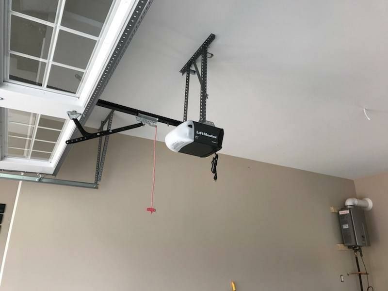 Garage door opener on a garage ceiling. The door is white. The walls are beige.