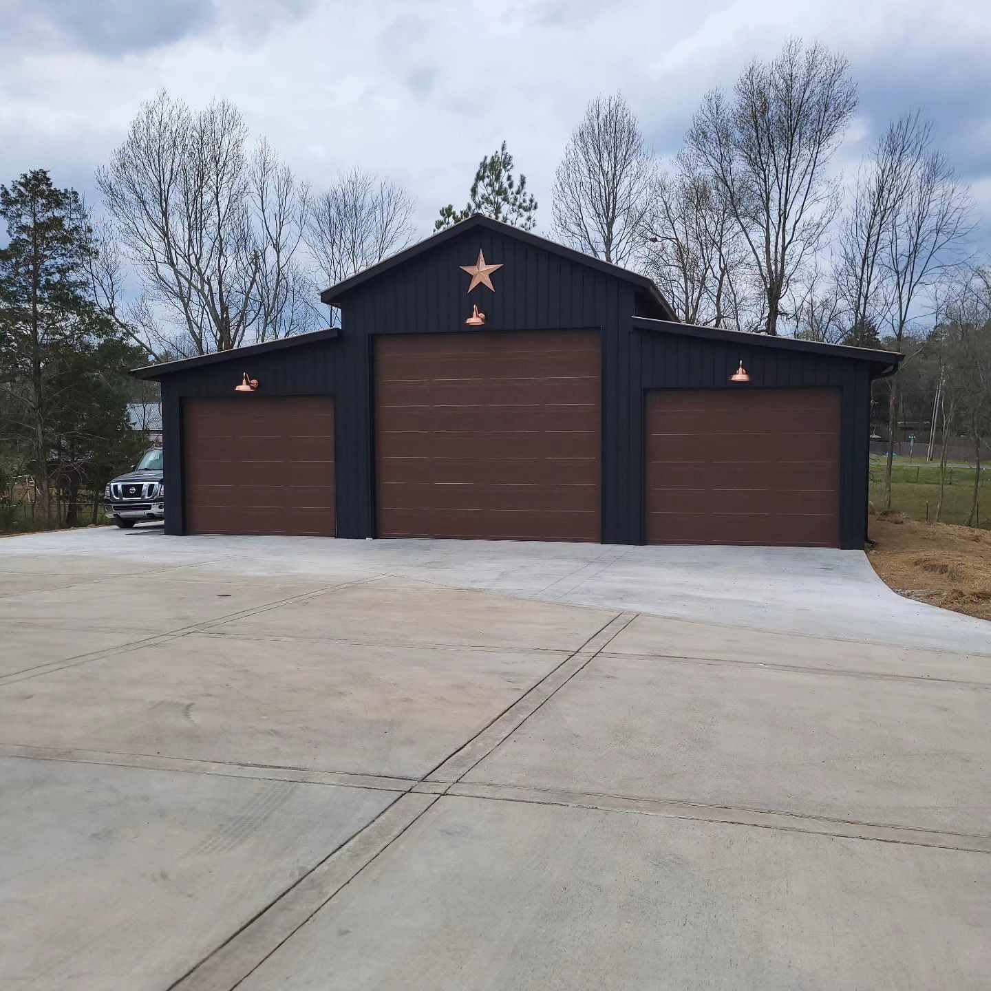 Three-bay dark blue garage with brown doors; concrete driveway; star decoration; overhead lights.