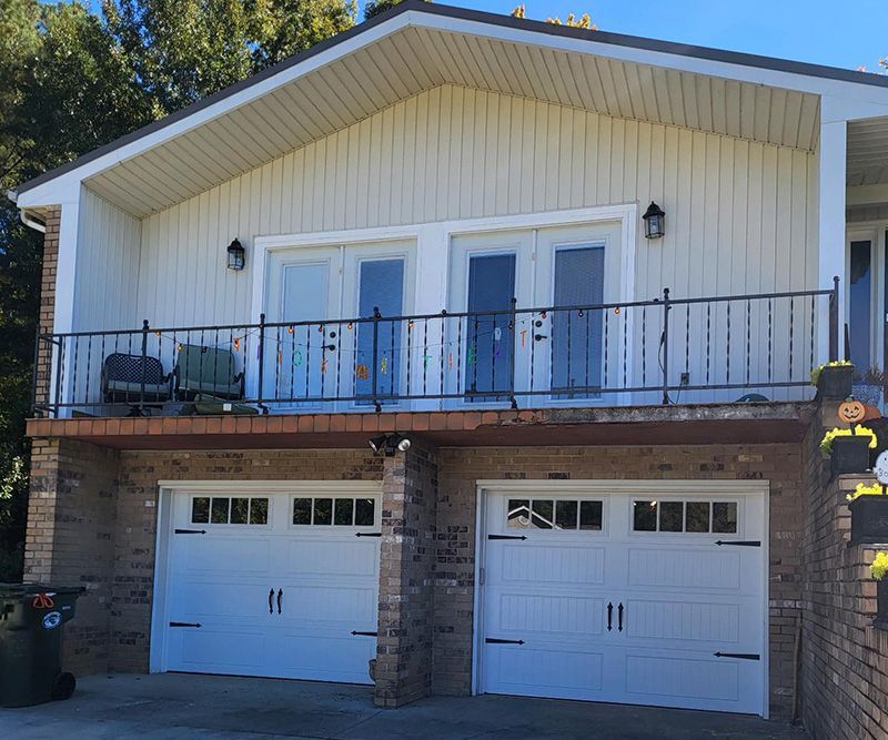 Two-story house with a garage. White garage doors, brick columns, and a balcony with French doors.