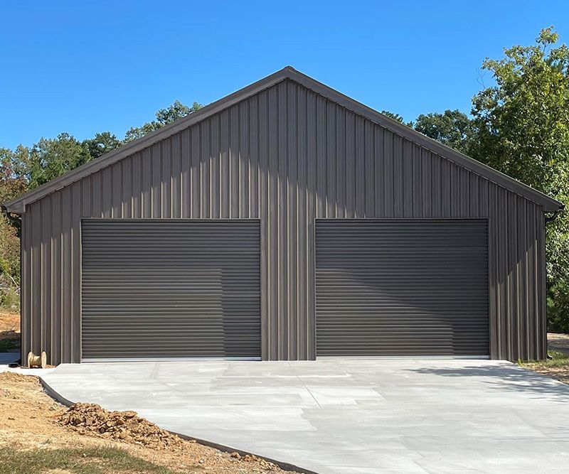 Two-car brown metal garage with concrete driveway, set against a blue sky and trees.