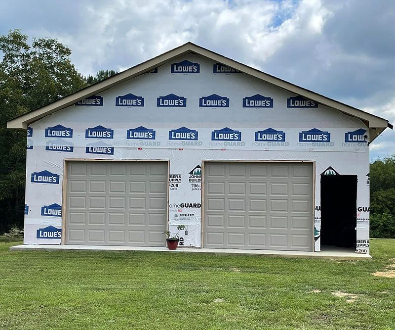 A two-car garage under construction; tan garage doors, Lowe's house wrap, green grass, cloudy sky.