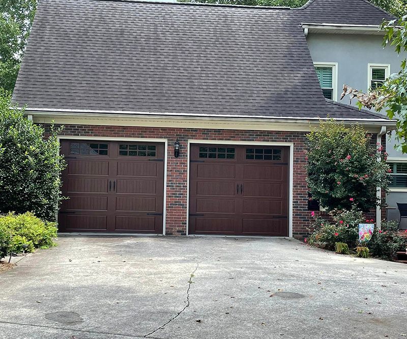 Brown garage doors on a brick structure with a cracked driveway.