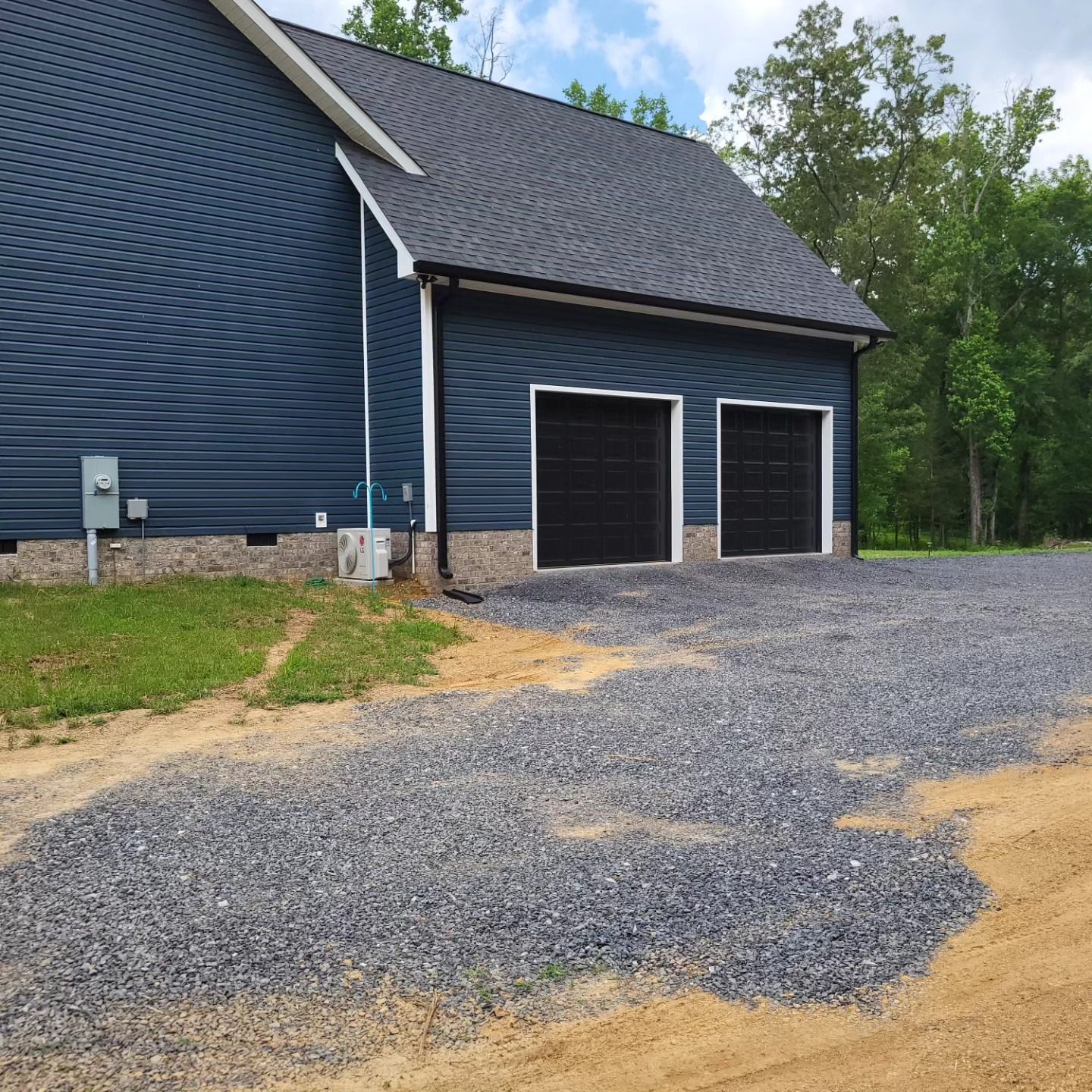 Blue house with two black garage doors, gravel driveway.