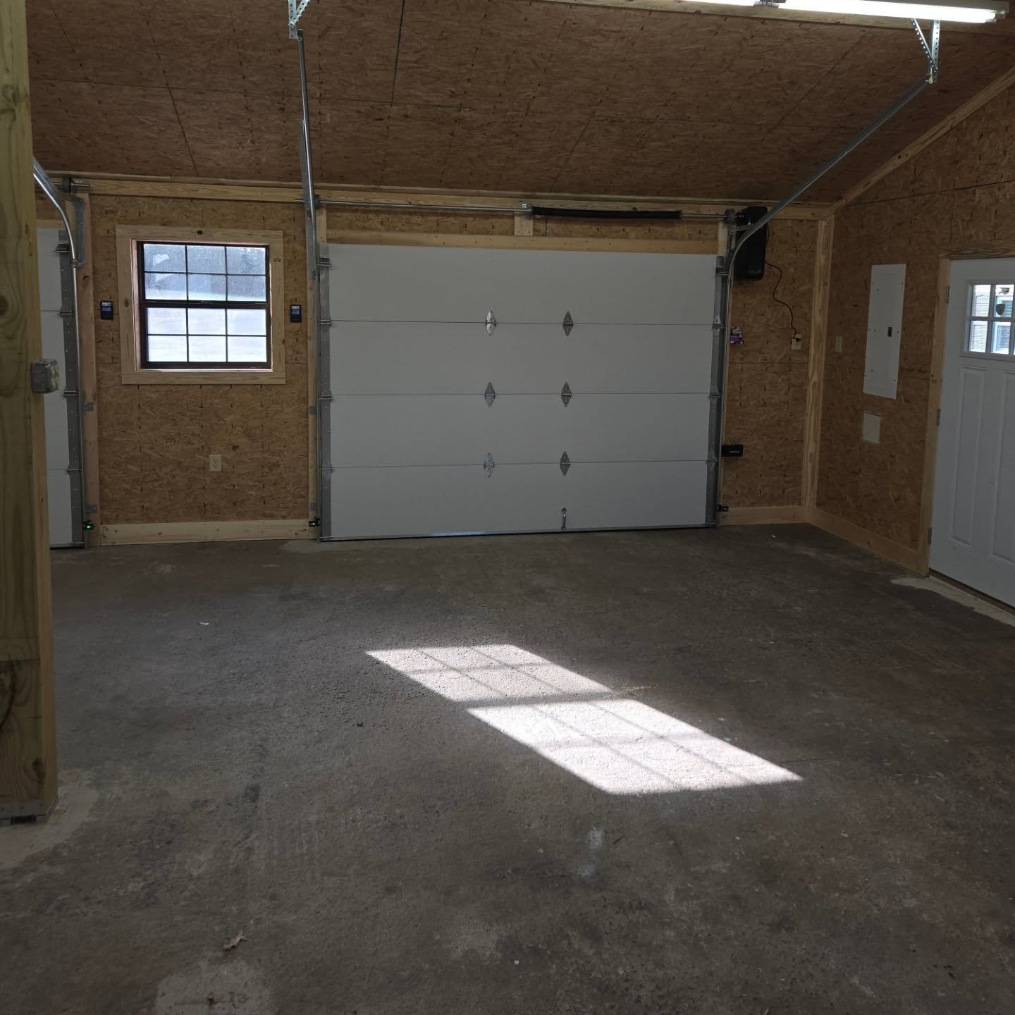 Empty garage interior with closed white garage door and concrete floor. Sunlight streams across floor.