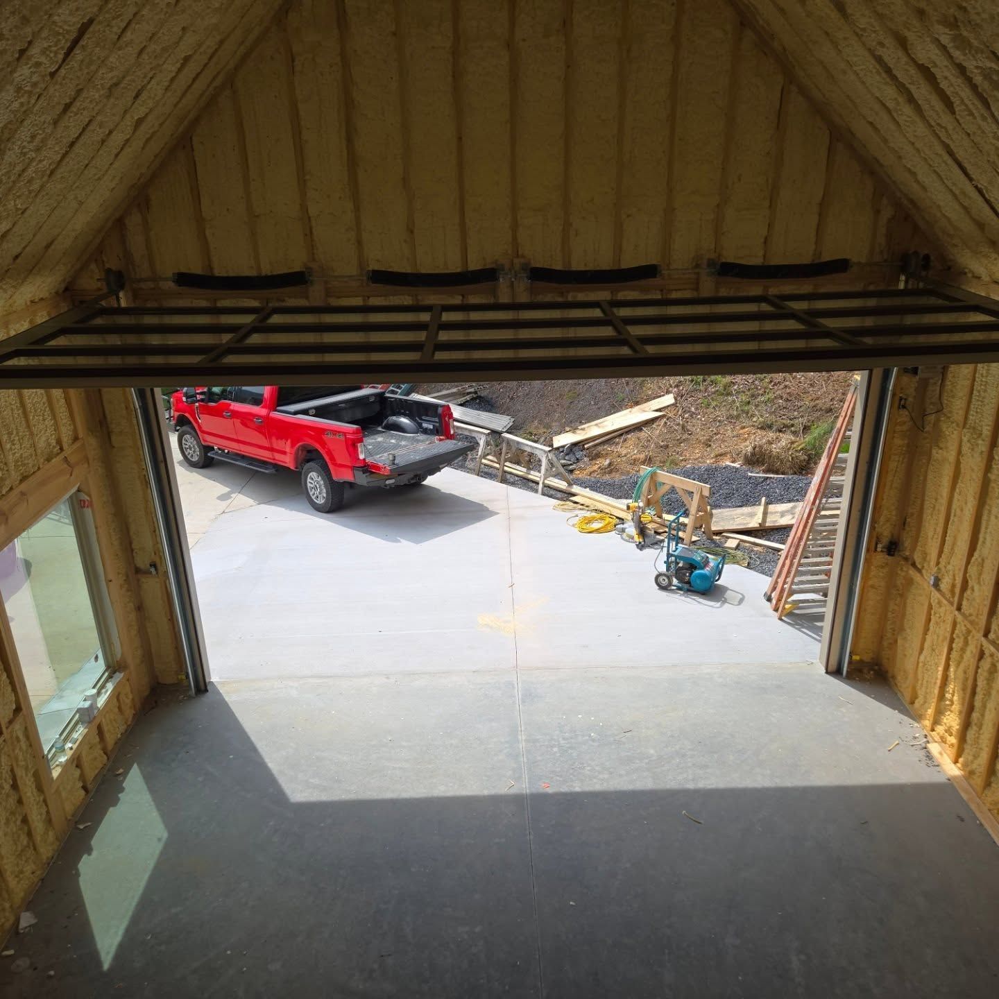 Inside view of a garage with a red truck parked outside, with insulation visible.