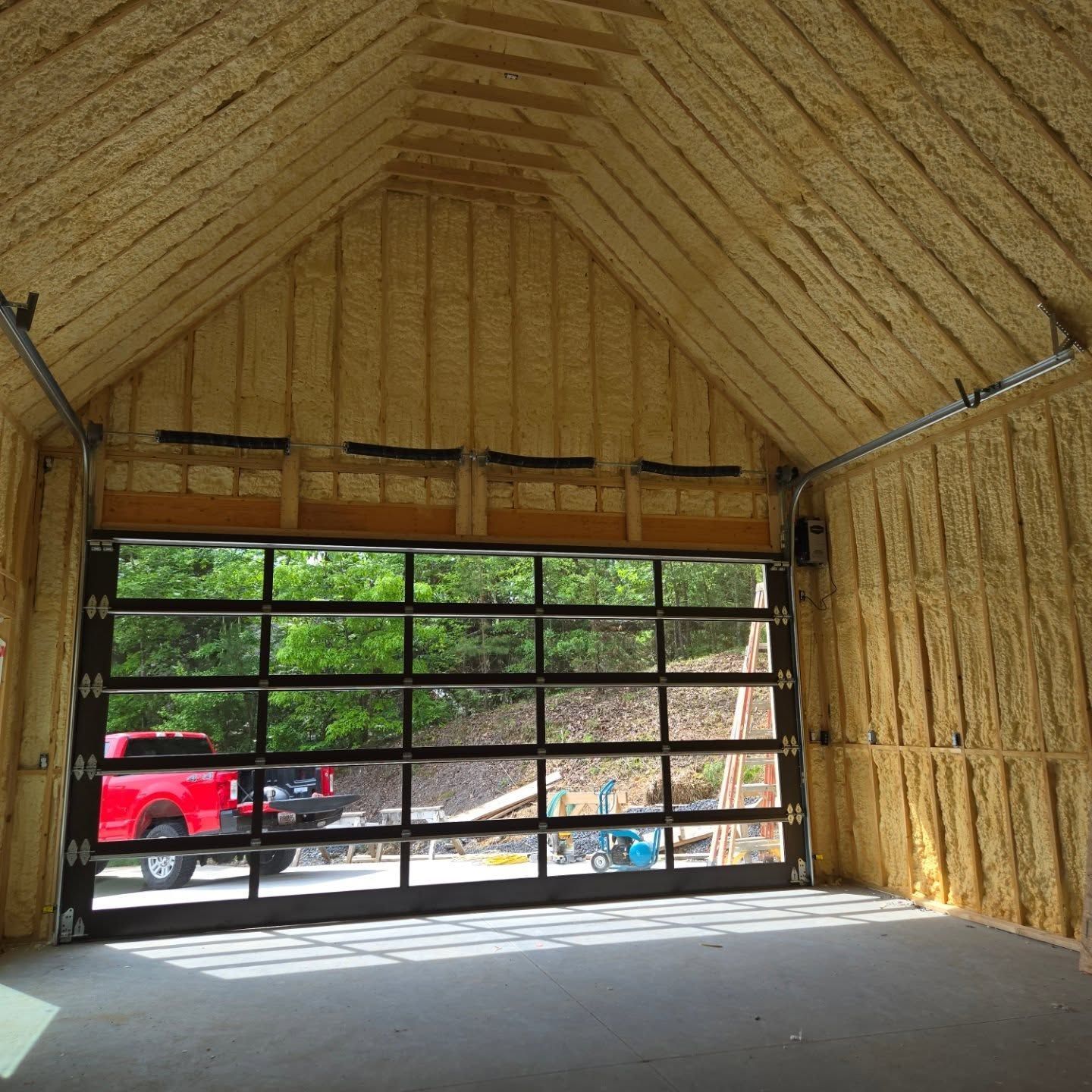 Interior of a garage with glass door. A red truck is visible outside. Walls and roof are insulated with spray foam.