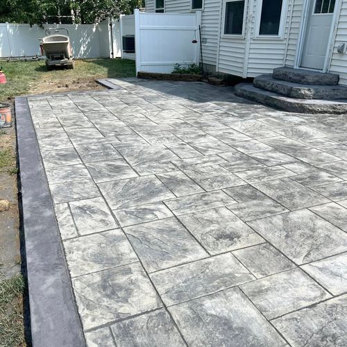 Gray brick patio next to a white house with a concrete border.