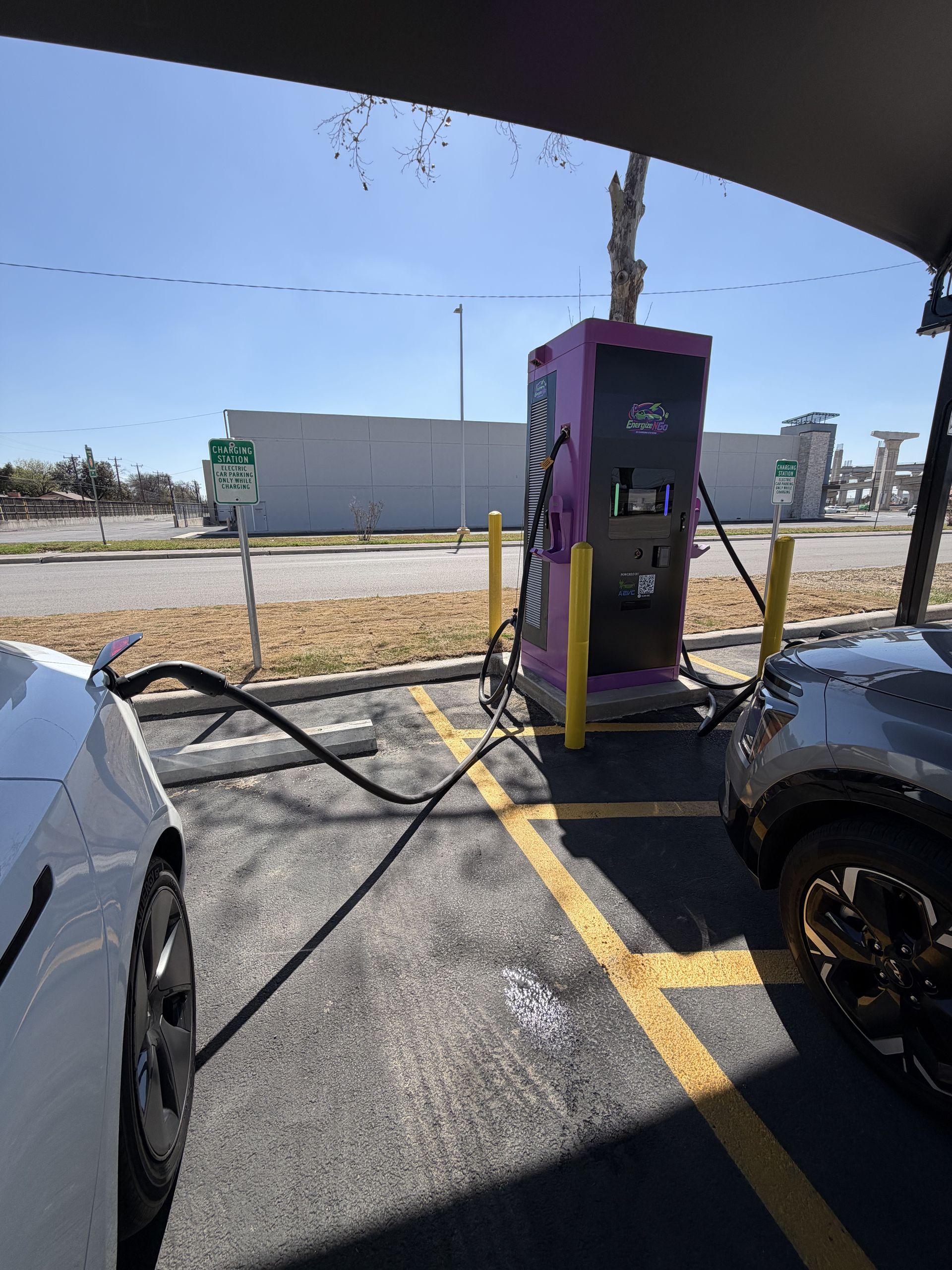 Electric vehicle charging station with purple charger and cars parked under a canopy on a sunny lot